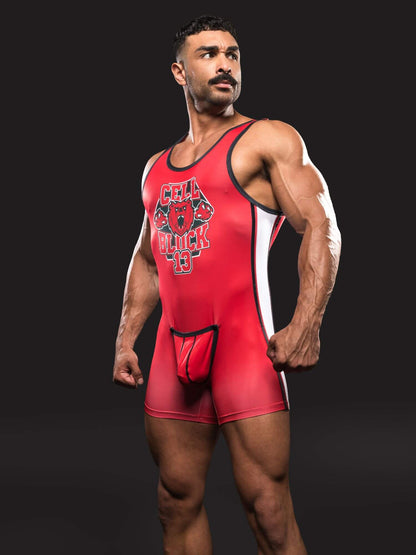 A muscular man modeling a red wrestling singlet with black and white trim, featuring a 'CELLBLOCK13' graphic on the chest, set against a dark studio background.