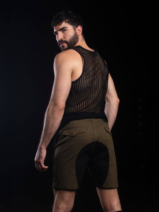 A man wearing a black mesh tank top and olive green shorts with black inner leg panels, photographed against a solid black studio background.