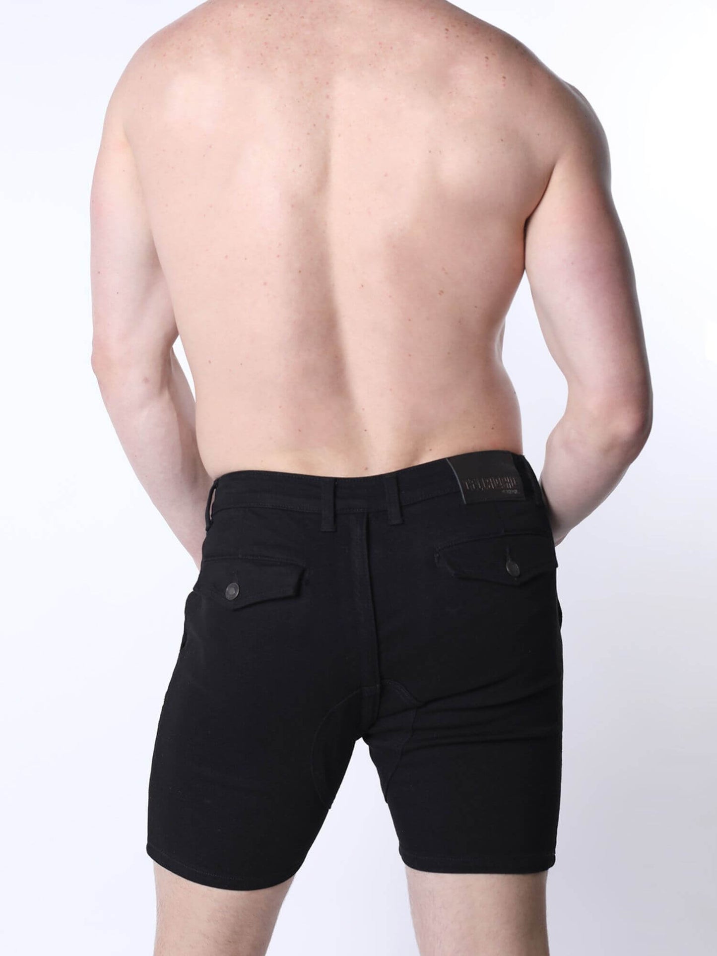 Rear view of a shirtless man wearing black denim shorts against a plain white background.