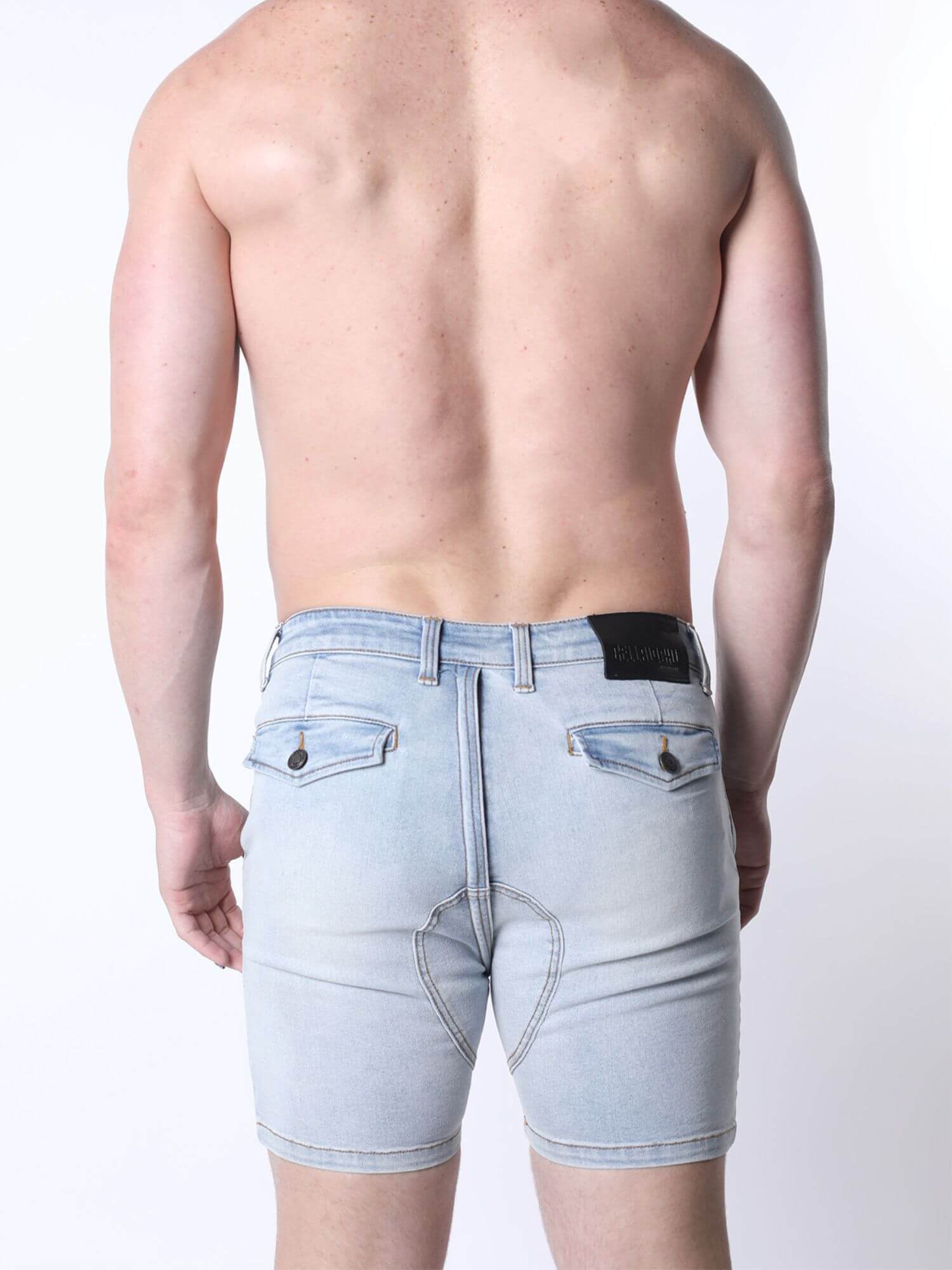 Rear view of a shirtless man wearing light-wash denim shorts against a plain white background.