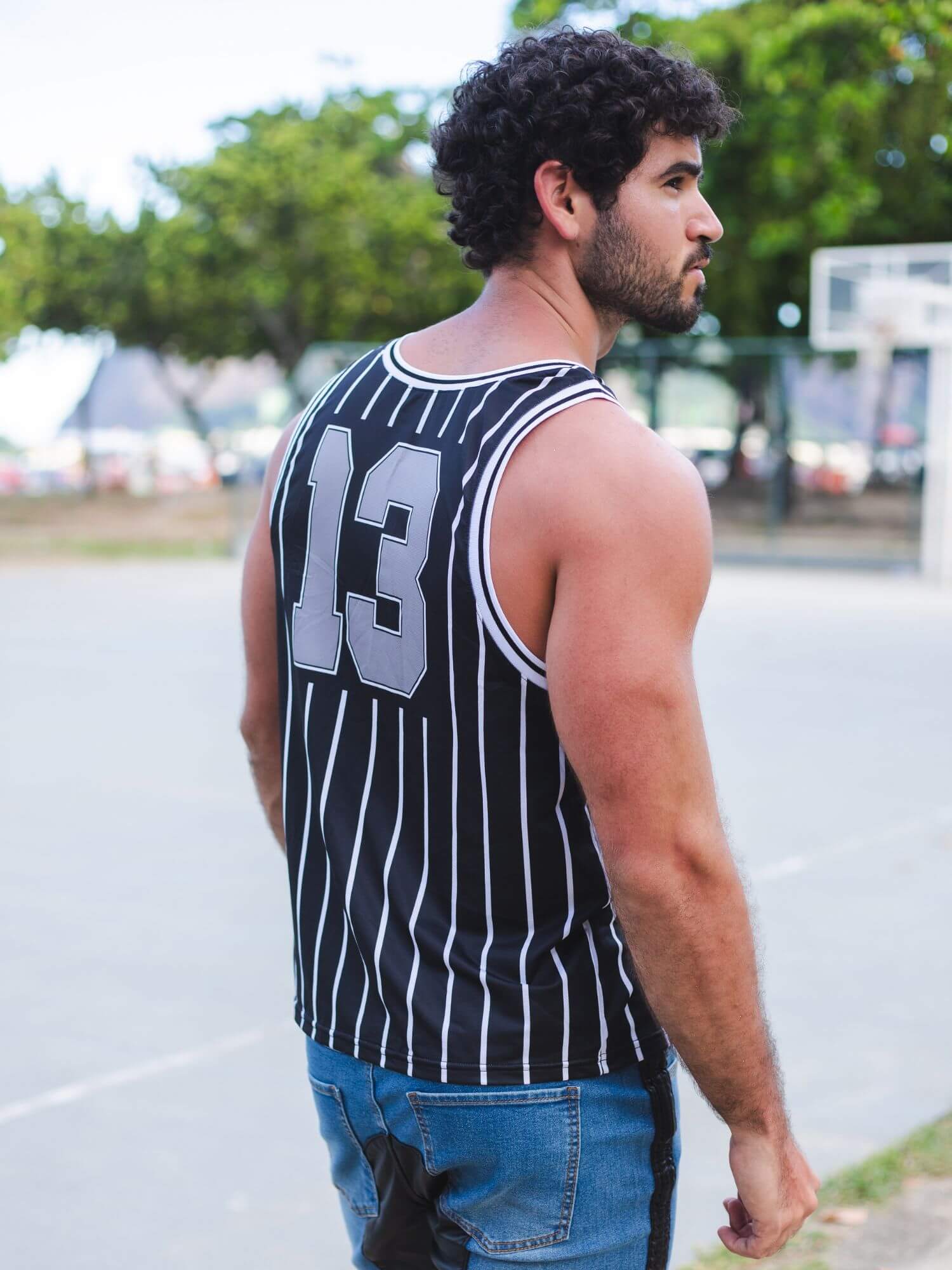 A man wearing a black and white vertically striped basketball jersey with the number 13 on the back, standing on an outdoor basketball court.