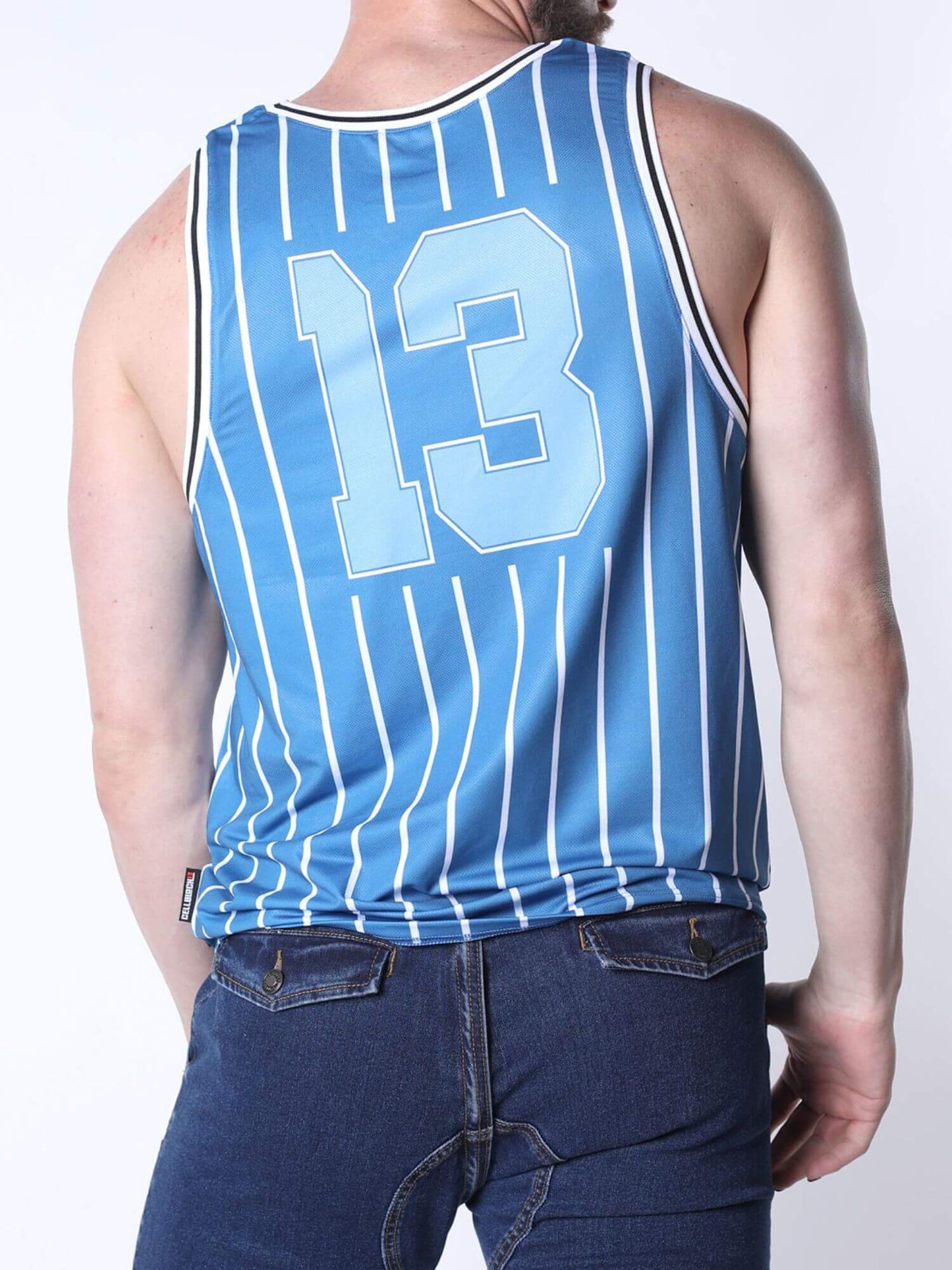 A man wearing a light blue pinstriped basketball jersey with the number 13 on the back, paired with dark blue jeans, shown from a rear three-quarter view against a white studio background.