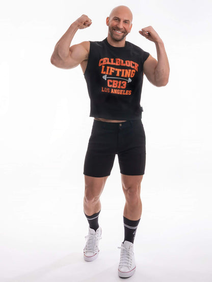 A muscular man posing in a black sleeveless tank top with orange and white 'CELLBLOCK LIFTING CB19 LOS ANGELES' text, paired with black shorts, black socks, and white sneakers against a white studio background.