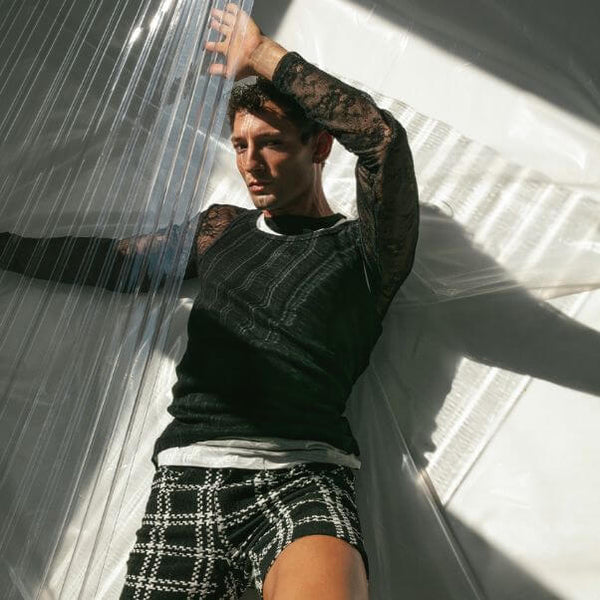Person wearing a black lace top and plaid shorts in a sunlit room.