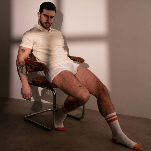 Man sitting on a chair wearing a white t-shirt, underwear, and socks with a minimal background