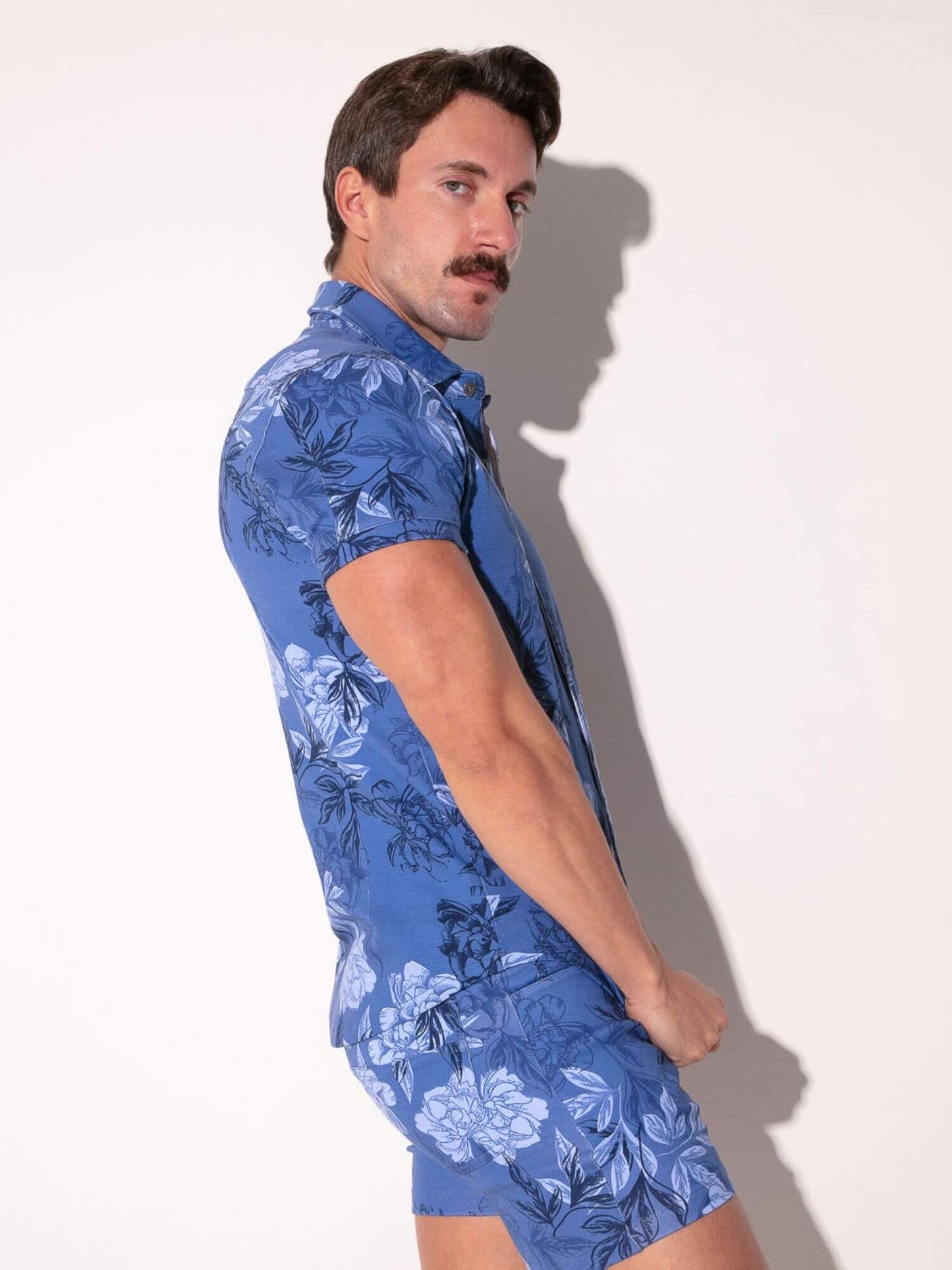 Man wearing a blue floral shirt and shorts against a white background