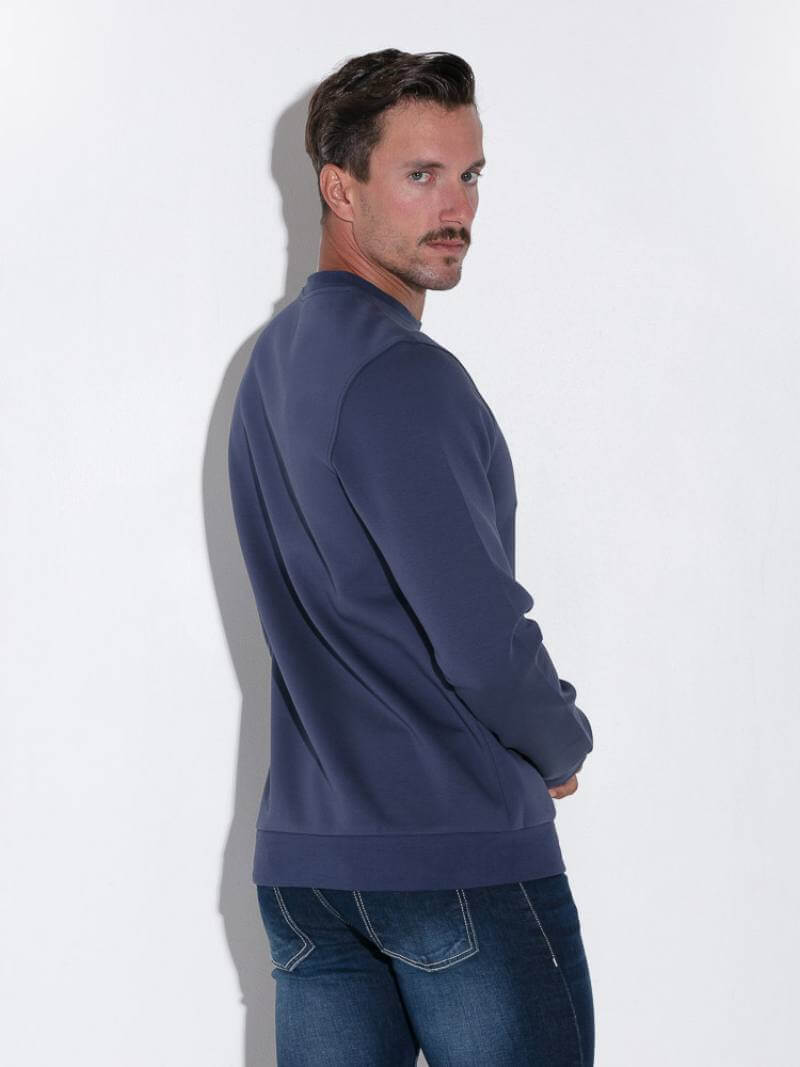 Man wearing a navy blue sweatshirt and jeans against a white background