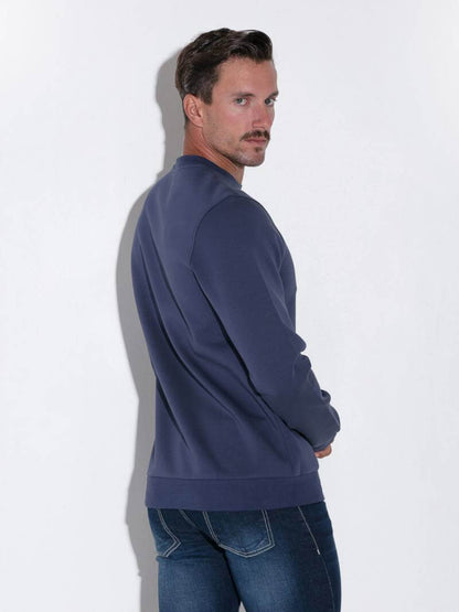 Man wearing a navy blue sweatshirt and jeans against a white background