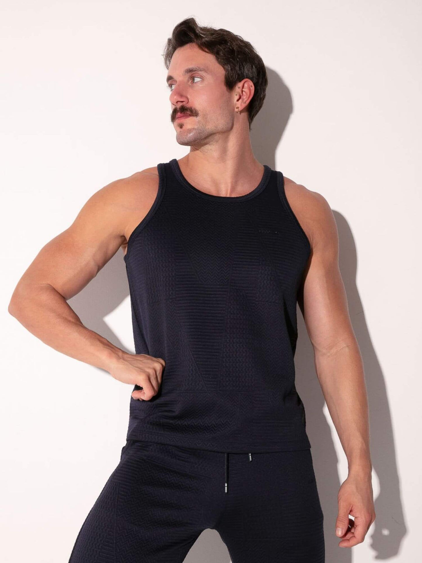 Man wearing a navy tank top and pants against a white background