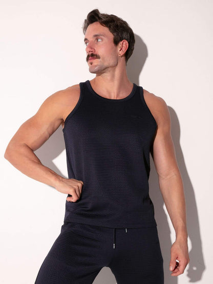 Man wearing a navy tank top and pants against a white background