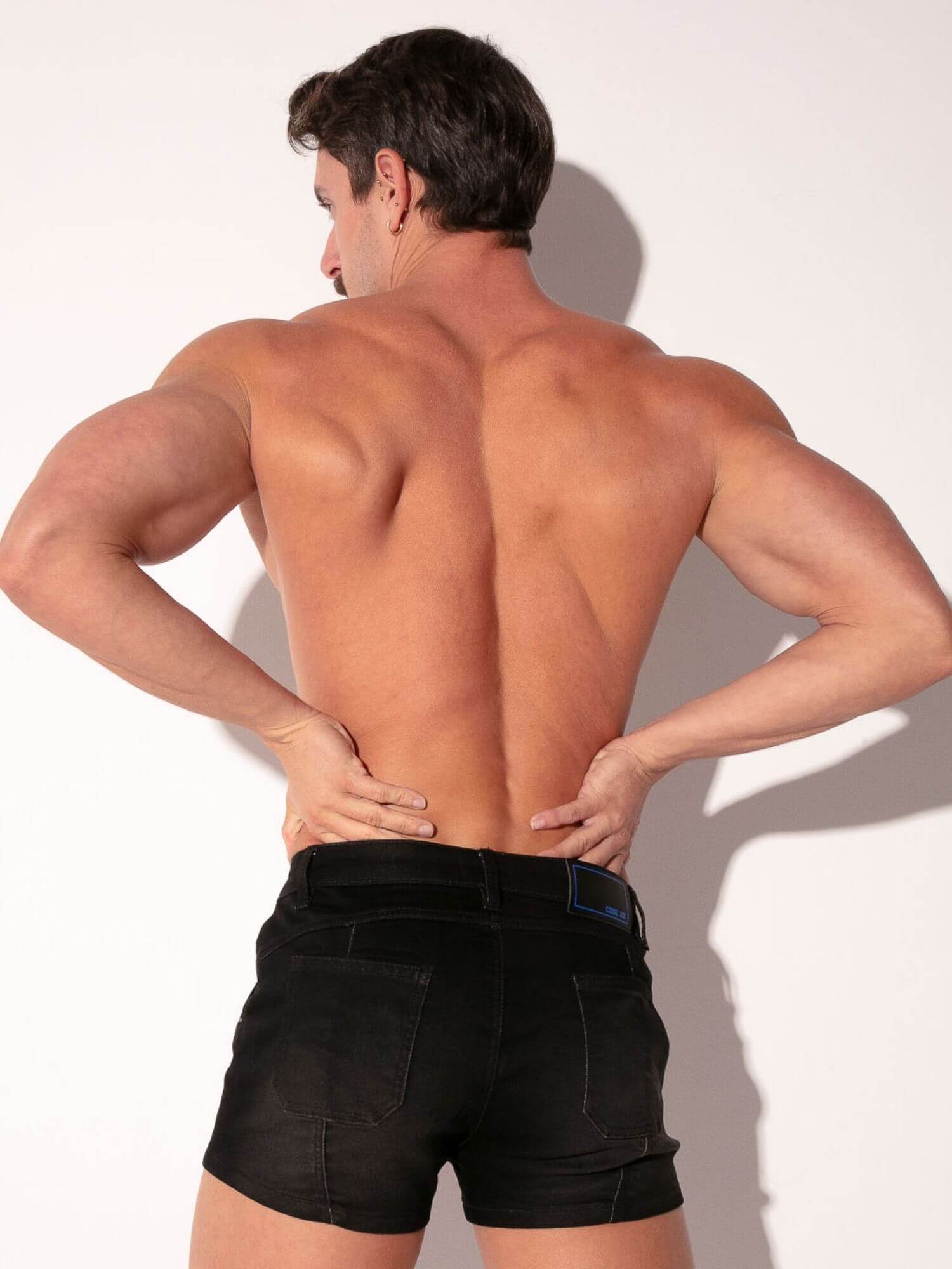 Man with muscular back and arms wearing black shorts against a white background