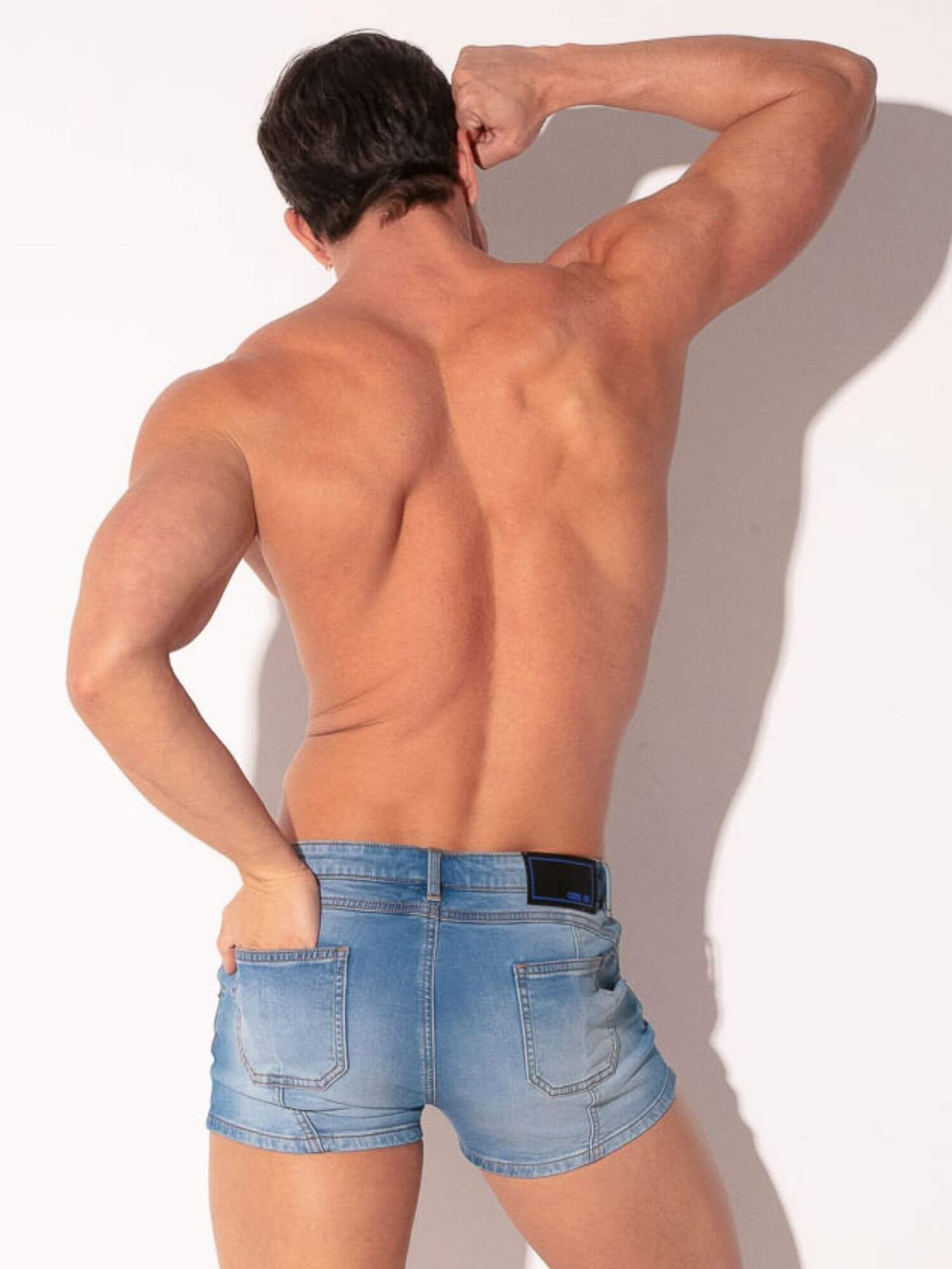 Man wearing light blue denim shorts with a plain background