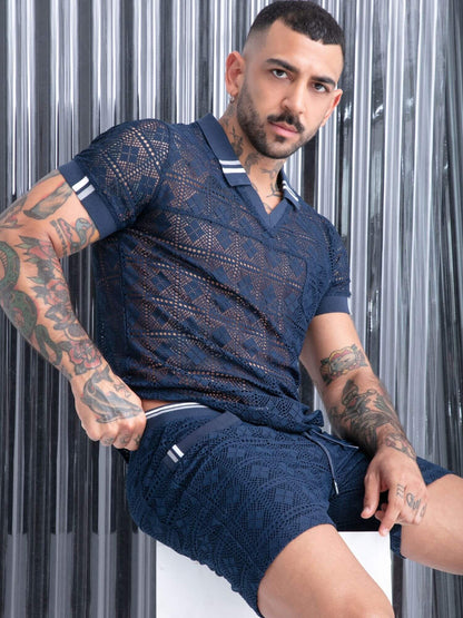 A man wearing a navy blue textured knit polo shirt and matching shorts, posing in front of a metallic silver corrugated backdrop.