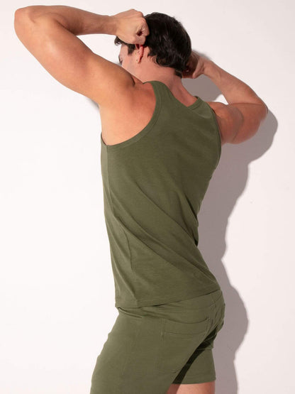 A man wearing an olive green tank top and matching shorts, shown from the back against a plain white wall.