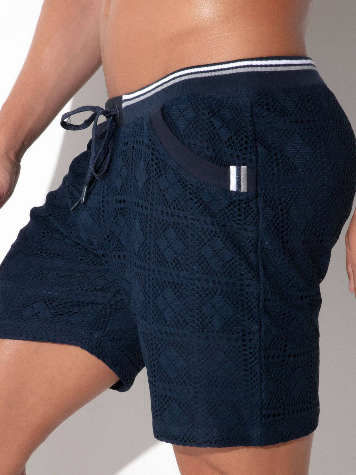 Close-up of a person wearing dark navy textured swim shorts with a white and navy striped waistband and a side pocket.