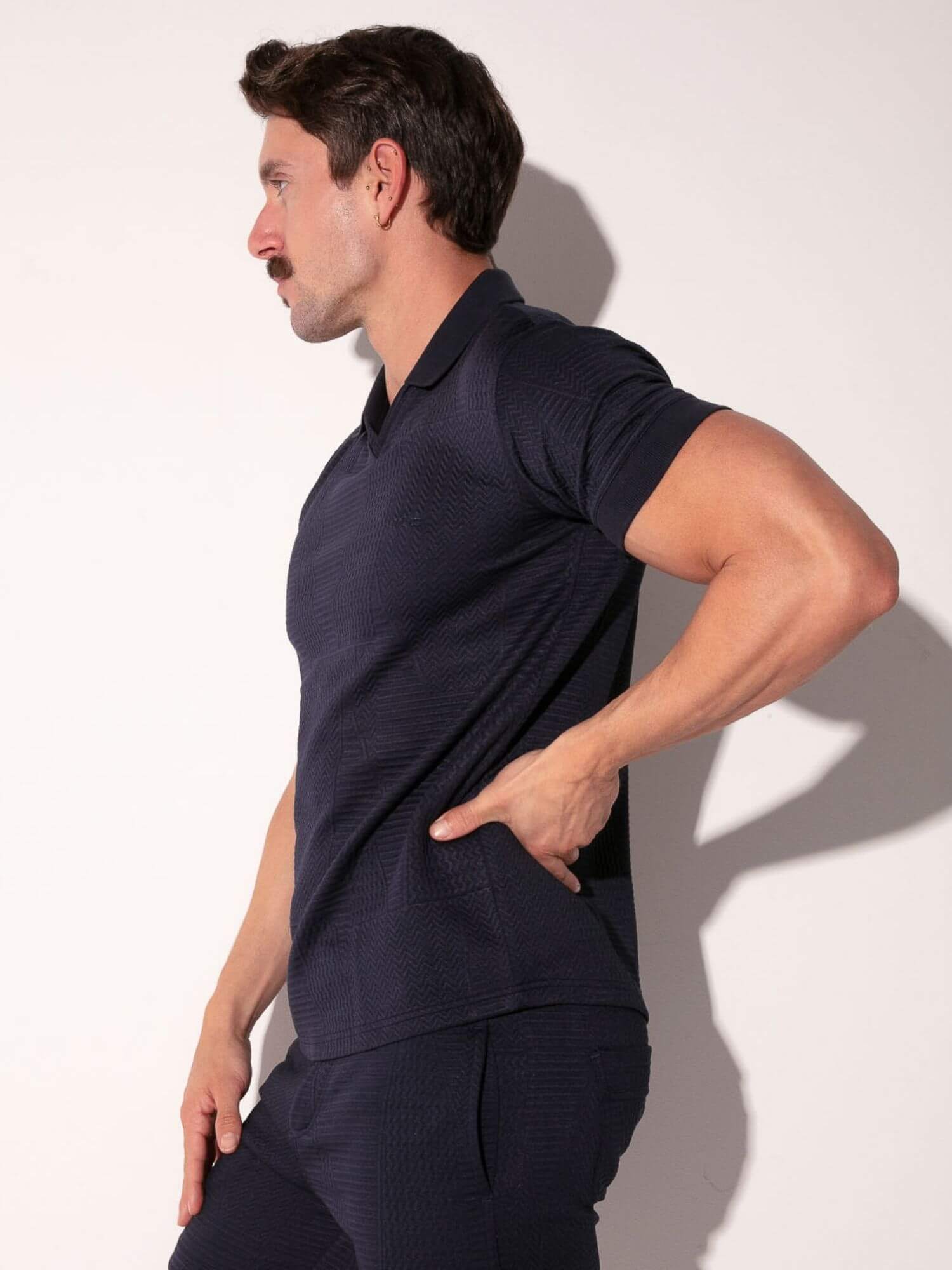 Man wearing a navy blue polo shirt and pants against a white background