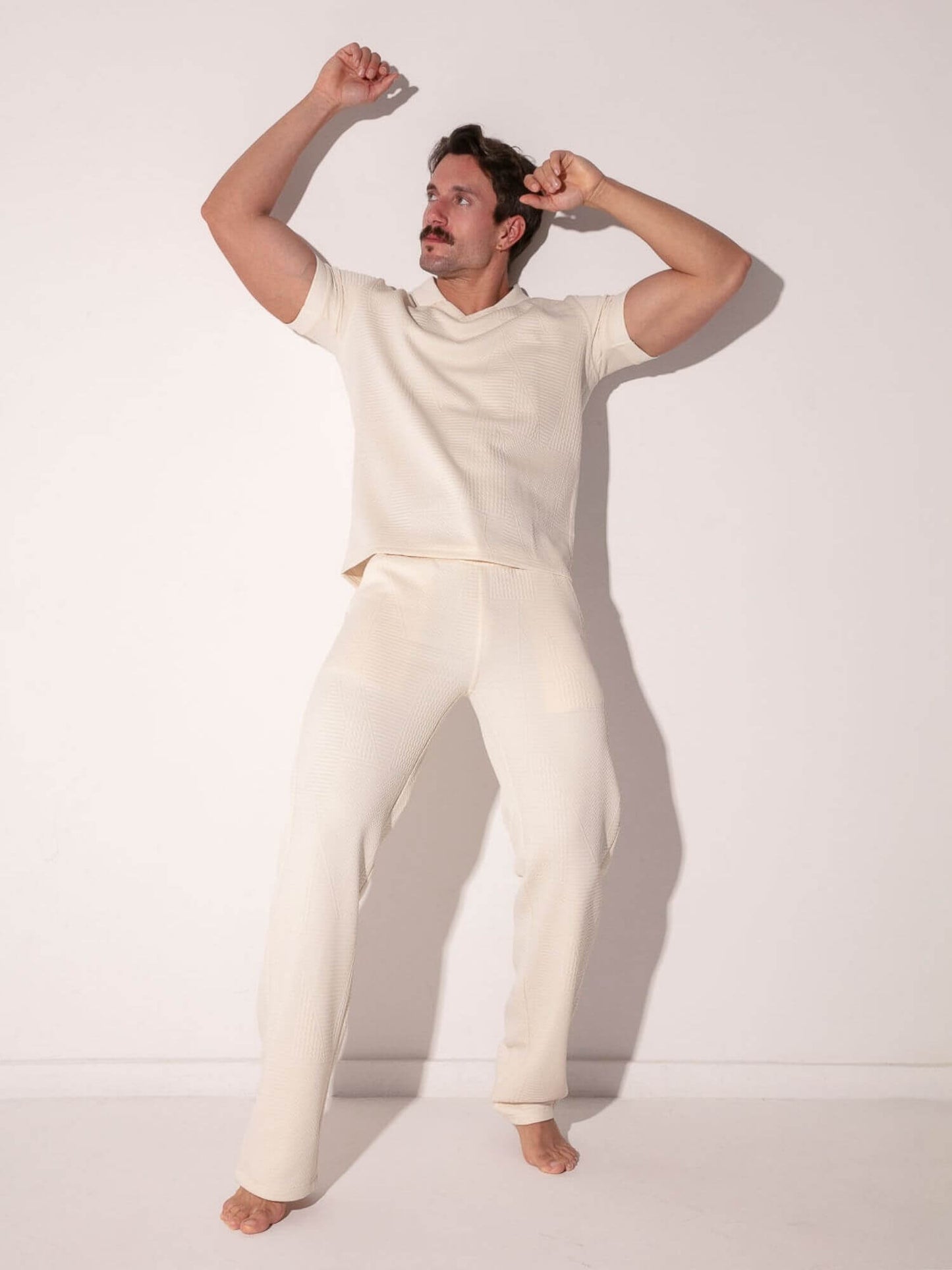Man wearing a off-white t-shirt and pants against a plain background
