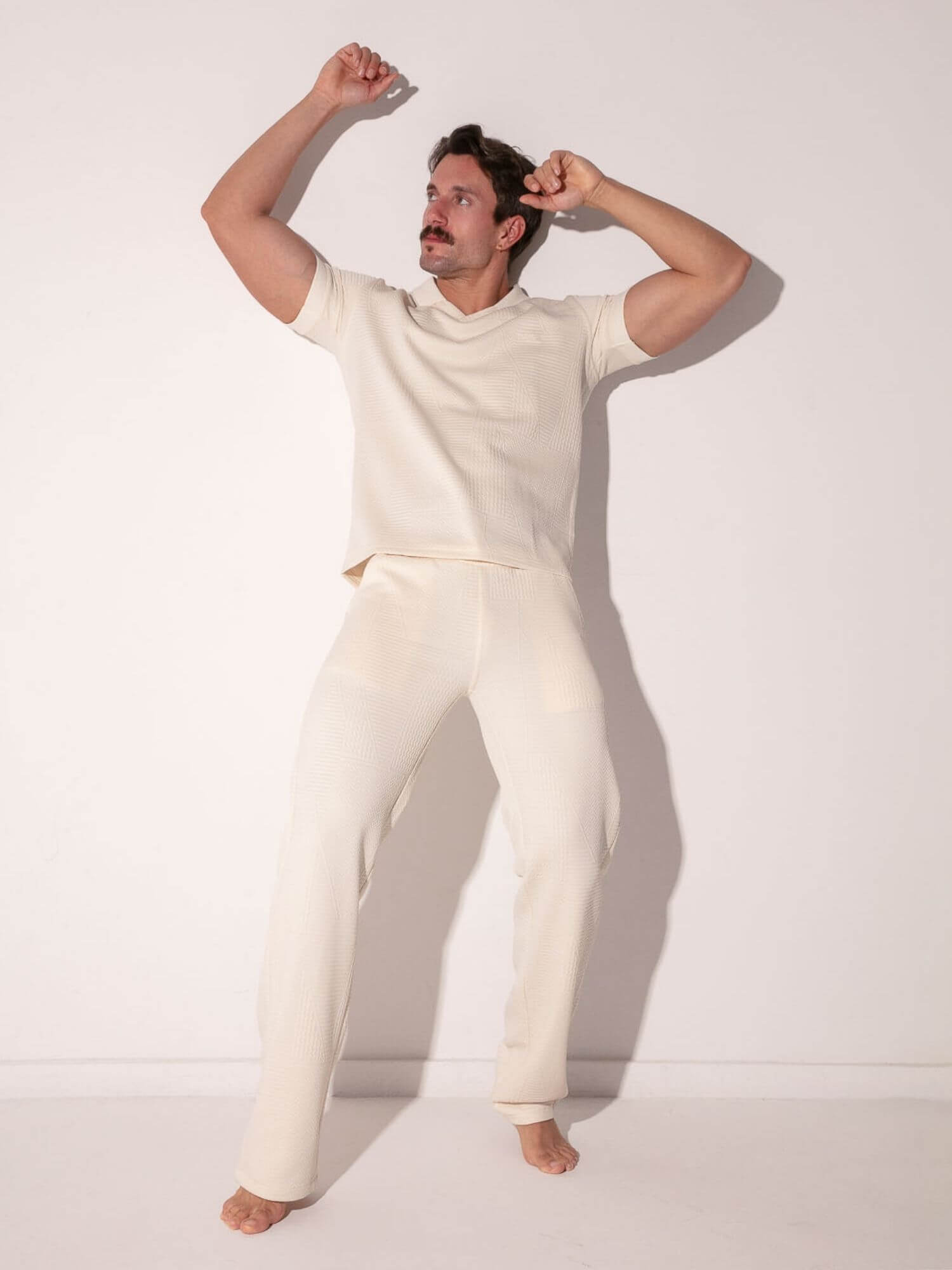 Man wearing a off-white t-shirt and pants against a plain background