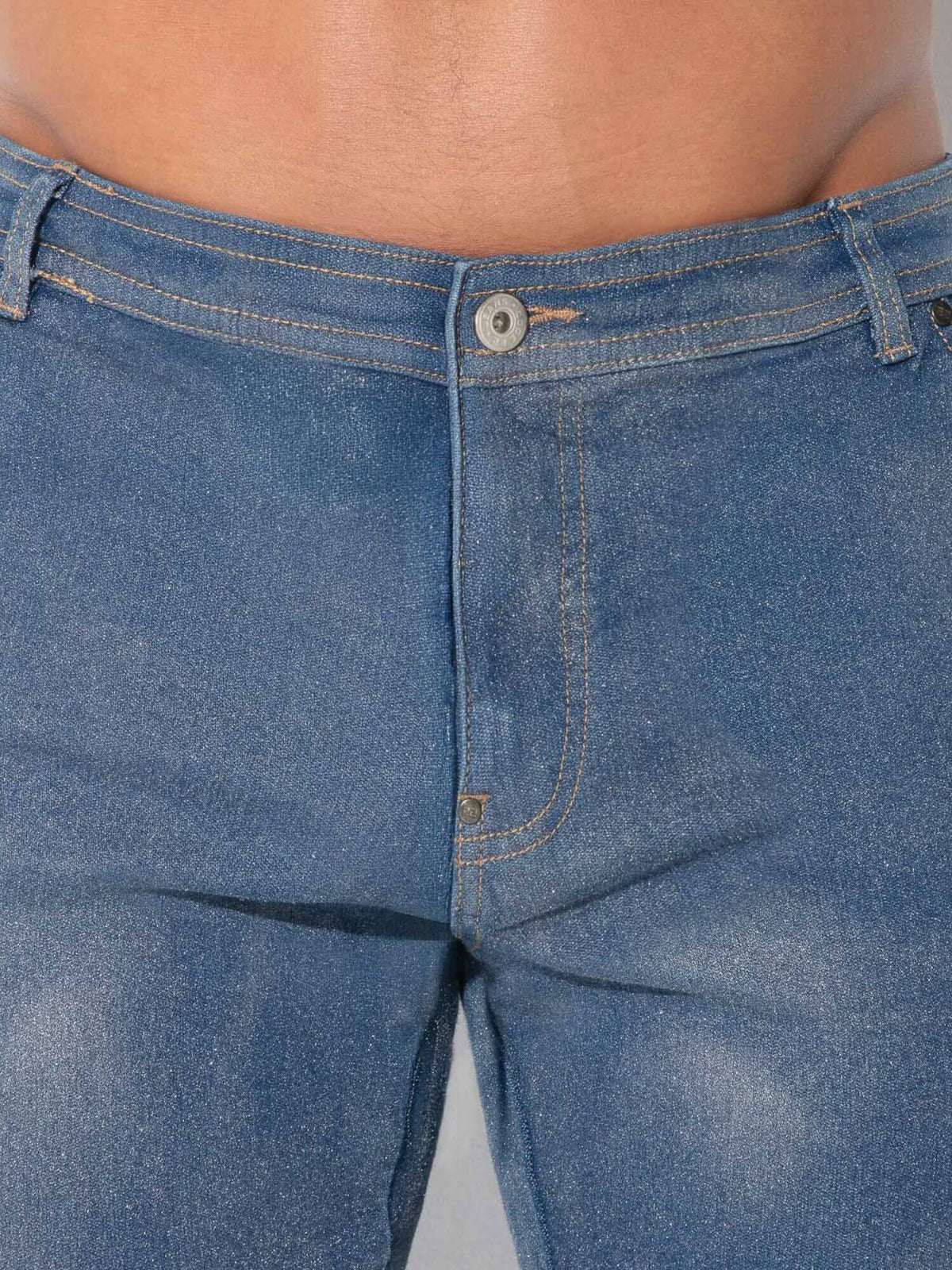 Close-up of a person wearing blue denim jeans, showing the waistband, button, front pocket, and thigh area against a plain light background.
