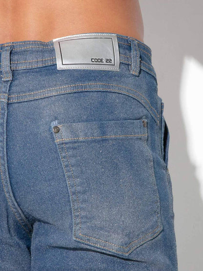 Close-up of the back waistband and pocket area of blue denim jeans worn by a model, showing a silver rectangular label that reads CODE 22.