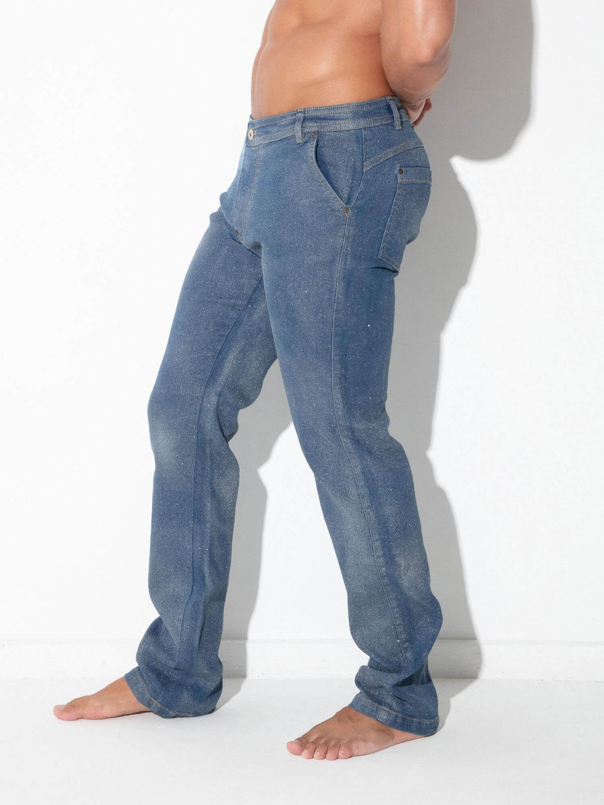 A man wearing blue denim jeans, shown from the waist down in a side profile against a white wall.