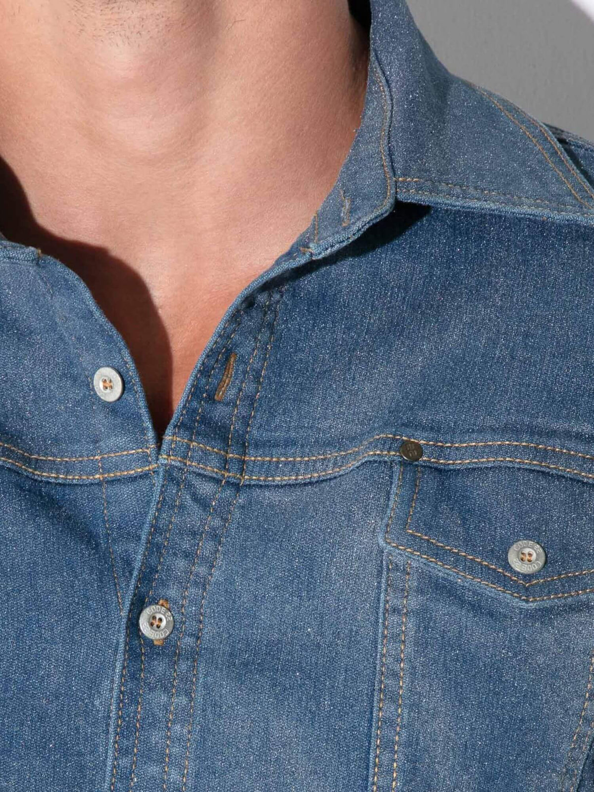 Close-up of a person wearing a blue denim button-up shirt, showing the collar, chest pocket, and front buttons.