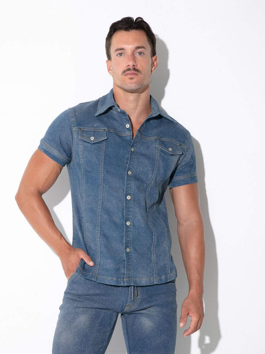 A man modeling a fitted short-sleeve blue denim shirt with matching blue jeans against a plain white studio background.