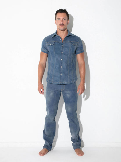 A man modeling a matching blue denim short-sleeve button-up shirt and jeans set against a plain white studio background.