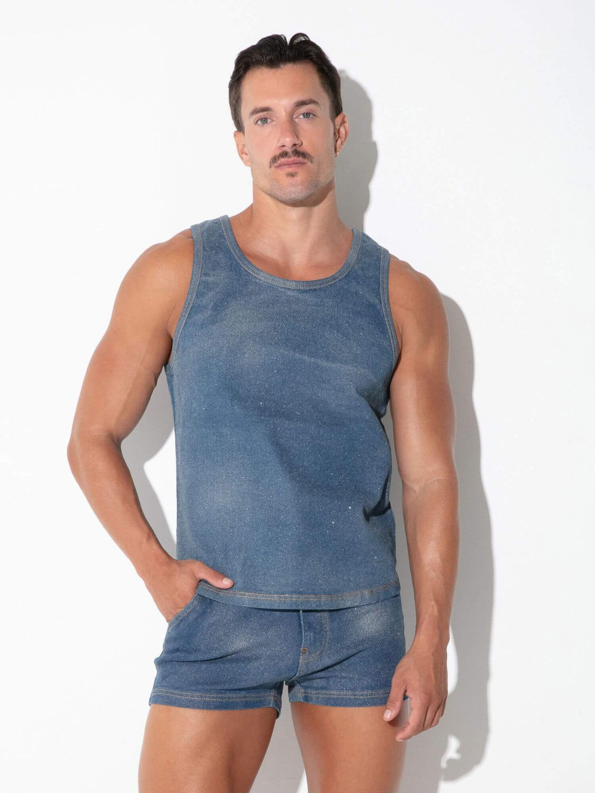 A muscular man modeling a matching blue denim tank top and shorts set against a plain white background with a soft shadow.