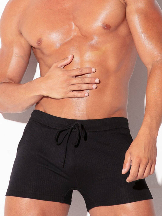 Man wearing black swim trunks with a neutral background