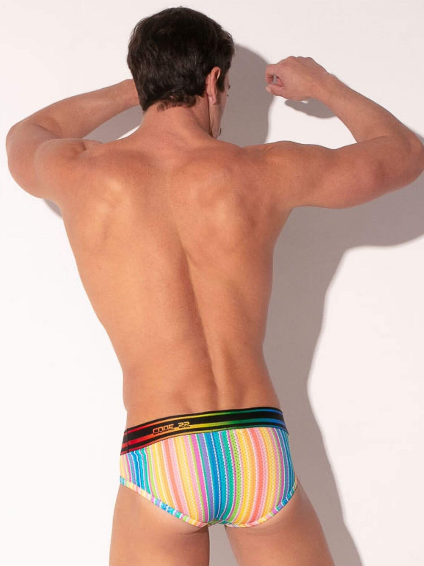 Man wearing colorful striped underwear with a rainbow waistband on a plain background