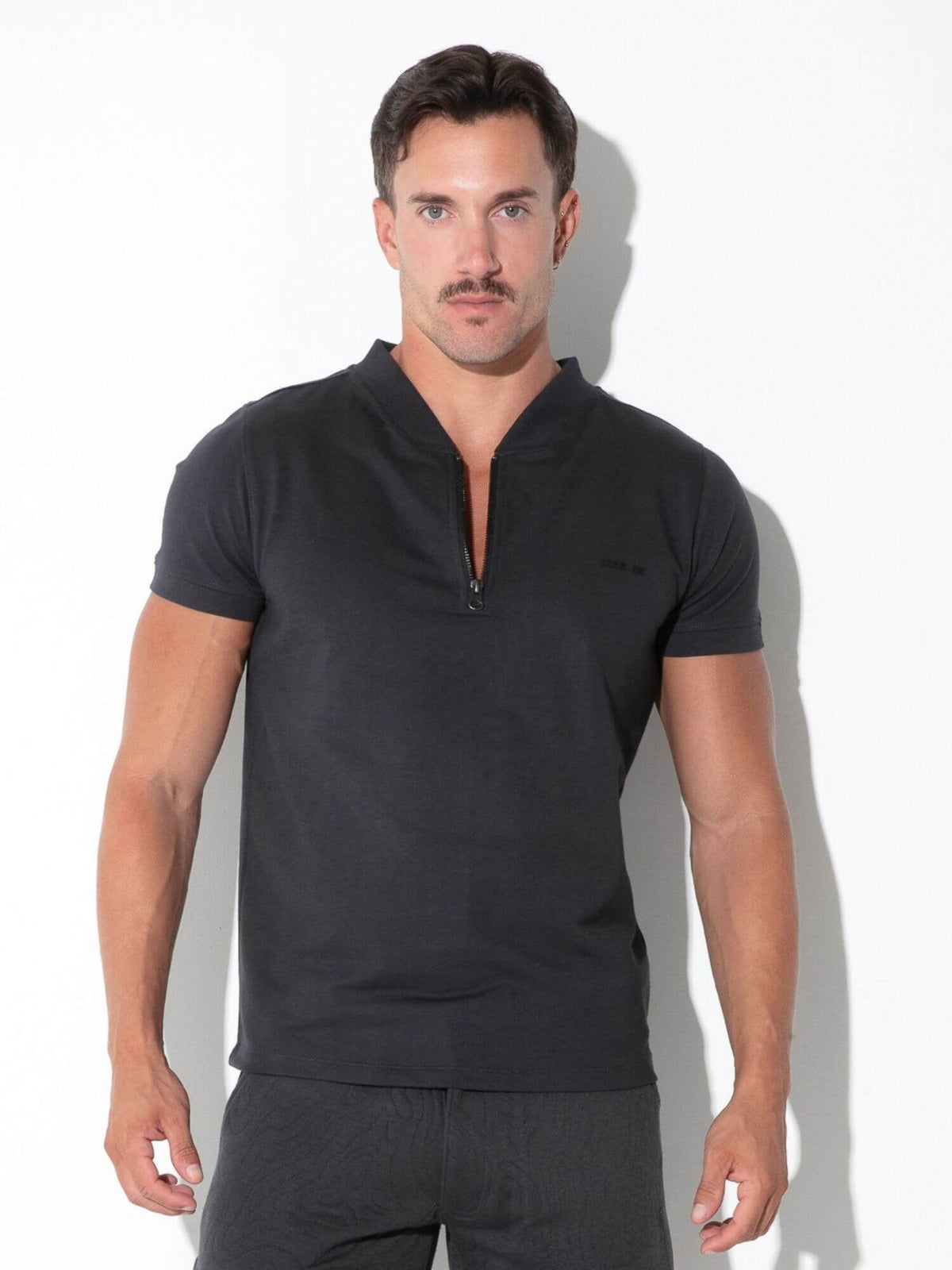 A man modeling a black short-sleeve half-zip polo shirt against a white studio background.