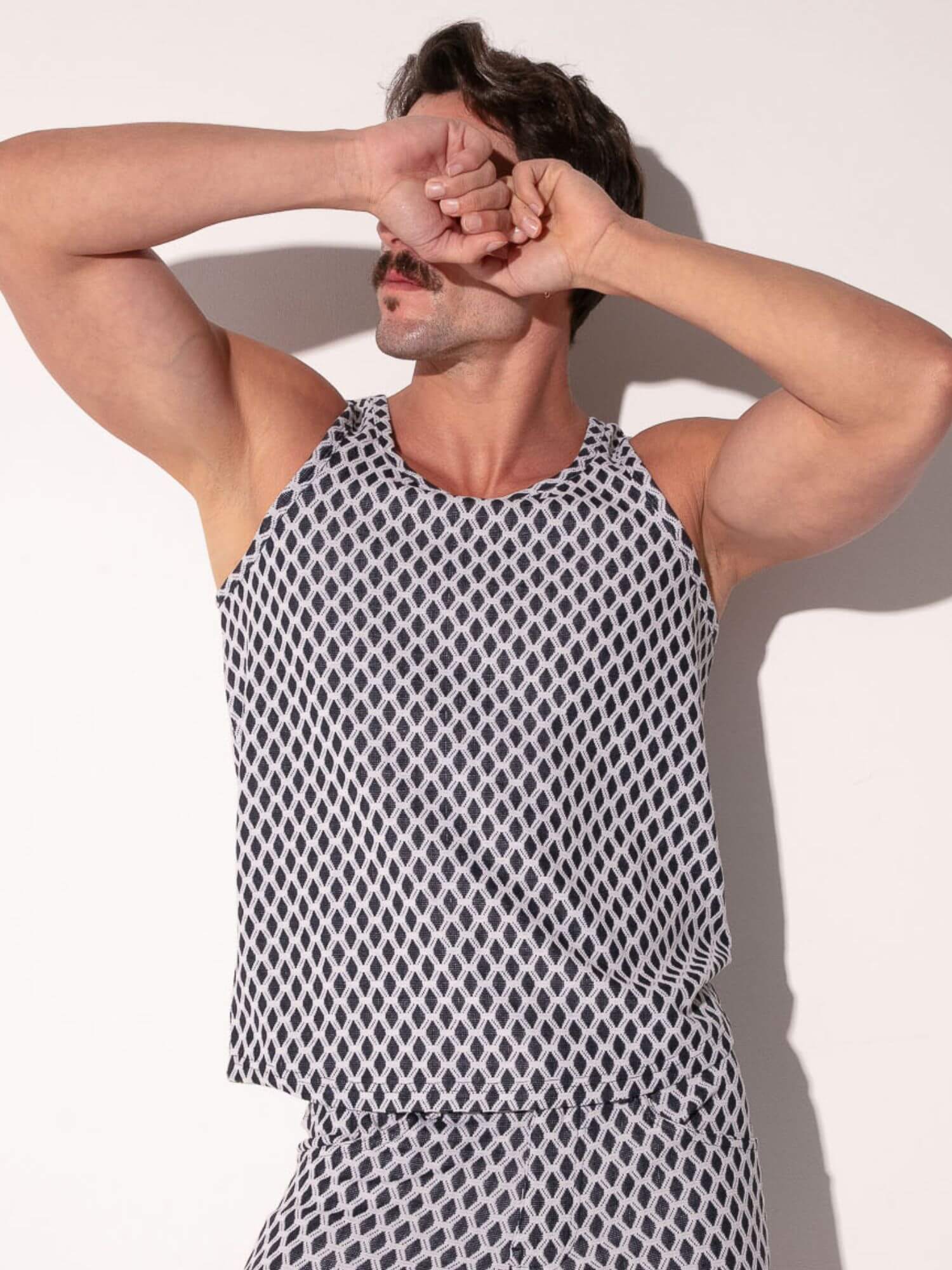 Man wearing a black and white patterned tank top against a light background