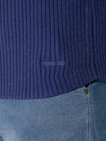 Close-up of a dark blue ribbed knit sweater hem with a small tonal 'code 22' logo, shown worn over blue jeans.