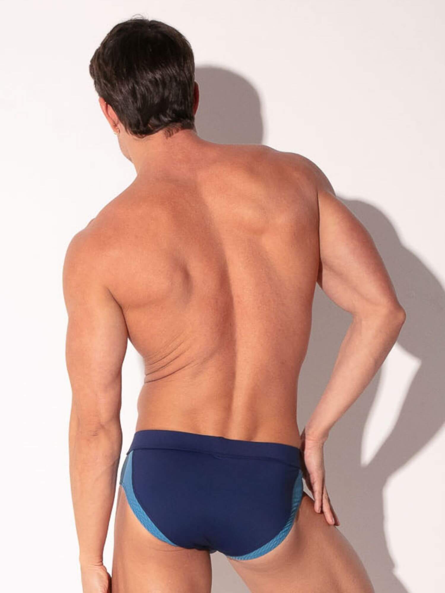 Man wearing navy blue swim briefs against a white background