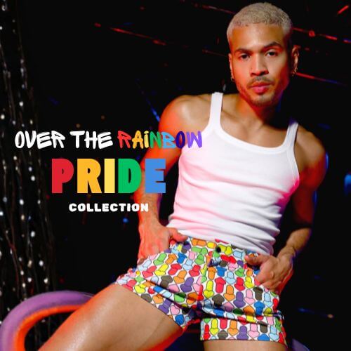 Person wearing a white tank top and colorful MODUS VIVENDI Rainbow Hearts shorts with 'Over the Rainbow Pride Collection' VOCLA pride menswear collection text.