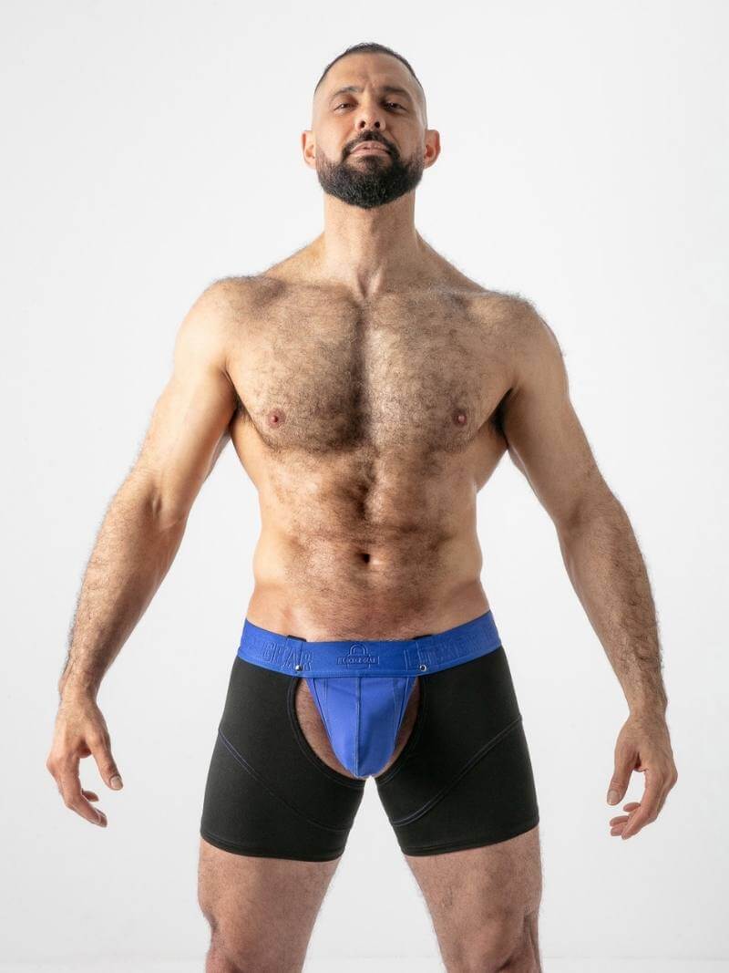 Man wearing black swim briefs with a blue jockstrap on a white background