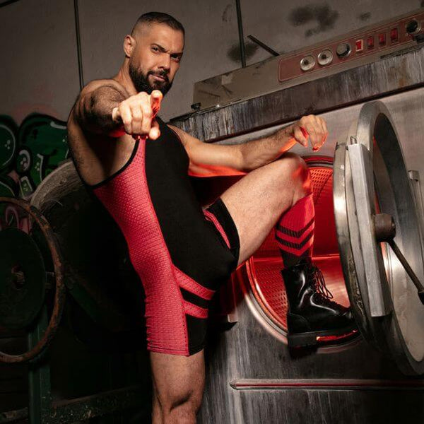 Man in red and black wrestling attire sitting on a weightlifting machine.