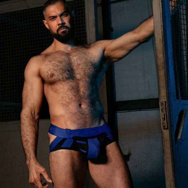Man wearing blue underwear standing against a metallic wall.