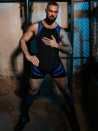 Man wearing a black and blue wrestling singlet in a dimly lit room.