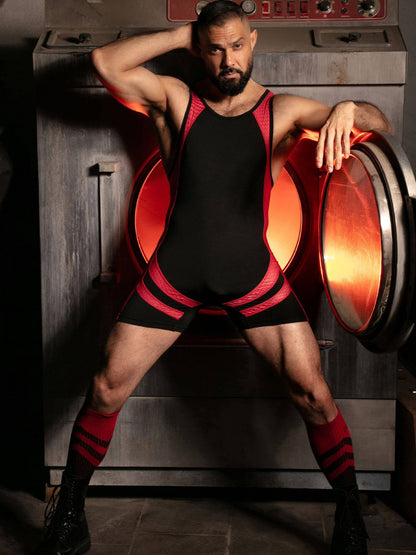 Person wearing a black and red outfit with large orange shoes in a dimly lit room.