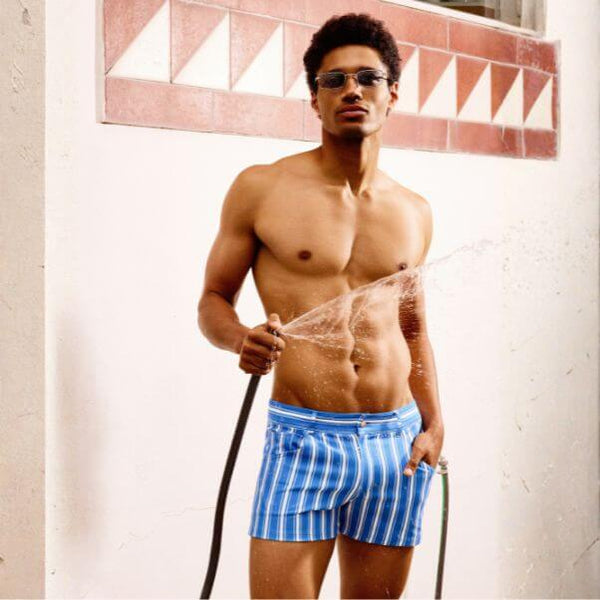 Man wearing blue striped MODUS VIVENDI Balanced shorts holding a hose indoors.