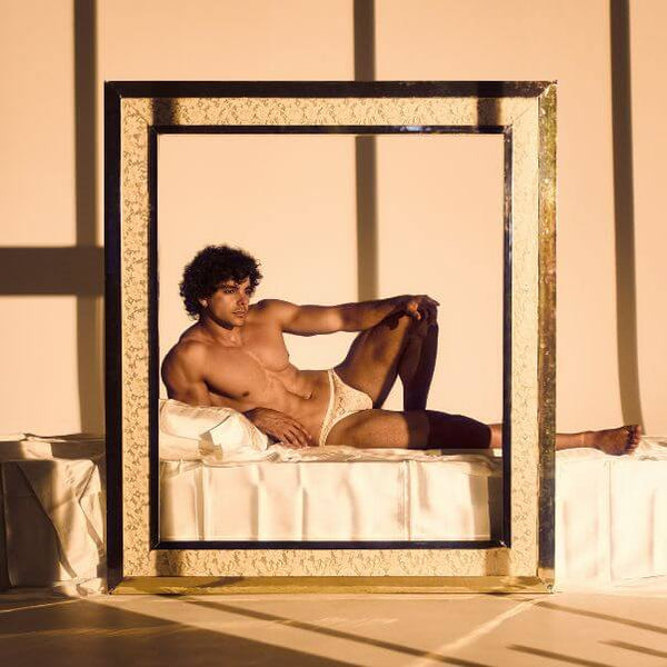 Man lying on a bed with a large decorative mirror casting a frame around him.