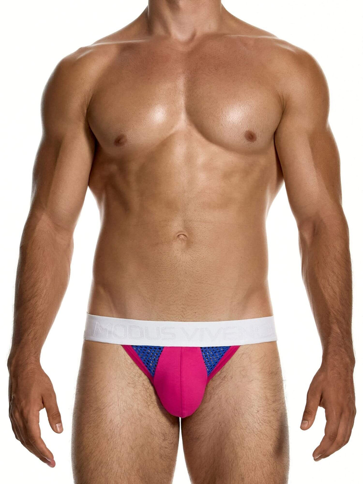 A muscular male model wearing a low-rise jockstrap with a bright pink pouch, blue mesh side panels, and a white waistband, set against a plain white background.