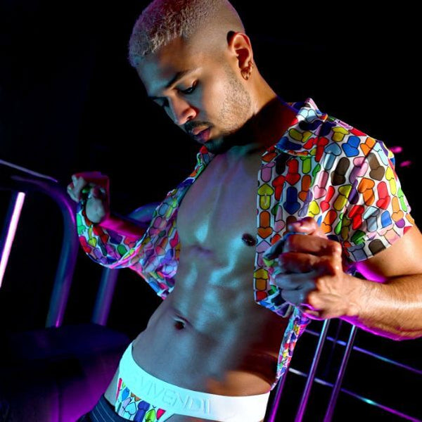 Man wearing a colorful MODUS VIVENDI rainbow pride patterned shirt and underwear against a dark background