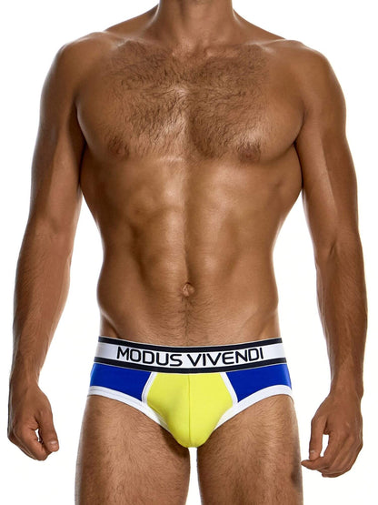 A male model wearing Modus Vivendi swim briefs with a yellow, blue, and white color-blocked design and a black waistband with white text.