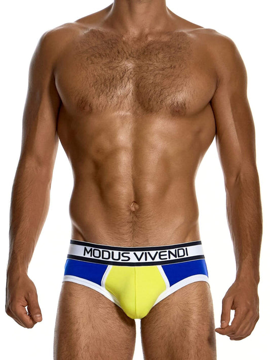 A male model wearing Modus Vivendi swim briefs with a yellow, blue, and white color-blocked design and a black waistband with white text.