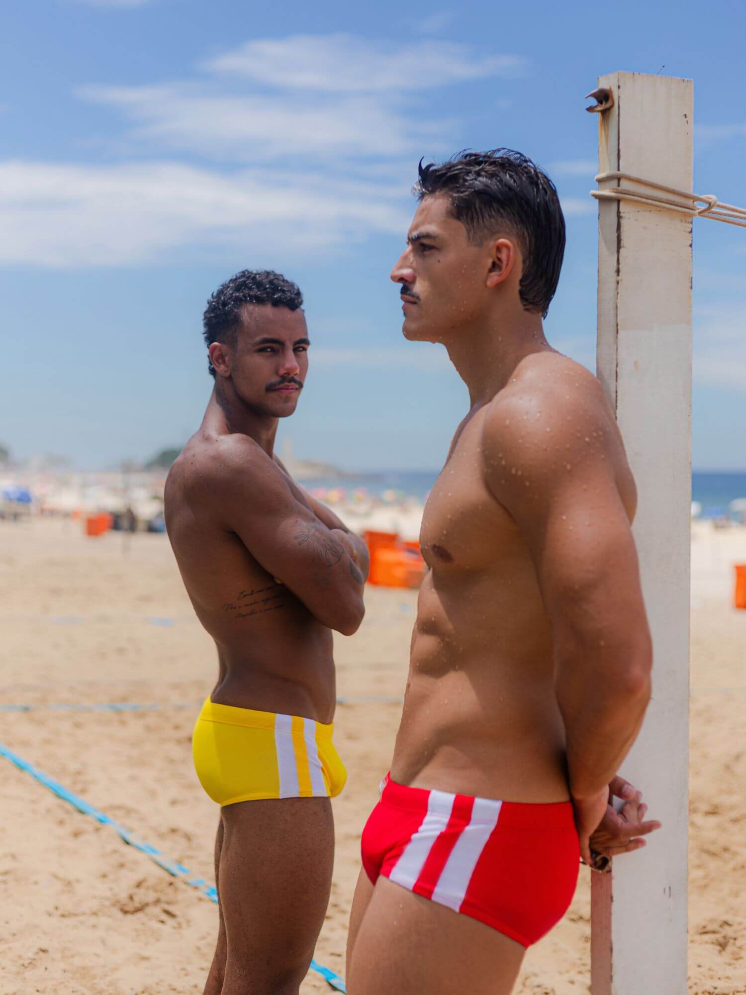 Two men standing on a beach wearing colorful swim trunks.