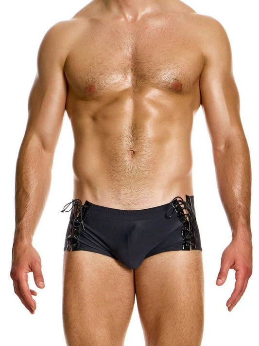 This image displays the MODUS VIVENDI Boudoir Brazil Cut Swim Trunk, featuring a smooth black fabric with shiny corset-style lace-up sides. The swim trunk is designed with a Brazil cut that includes super-short legs and a low-rise waist, offering a stylish and cheeky silhouette.