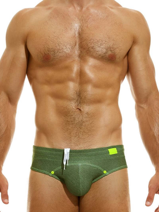 A model wearing a denim-inspired blue swim brief with press studs on the waistband and a silicone Modus Vivendi logo.